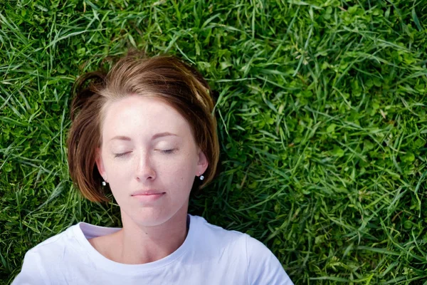 Красива дівчина з веснянками лежить на зеленій траві — стокове фото