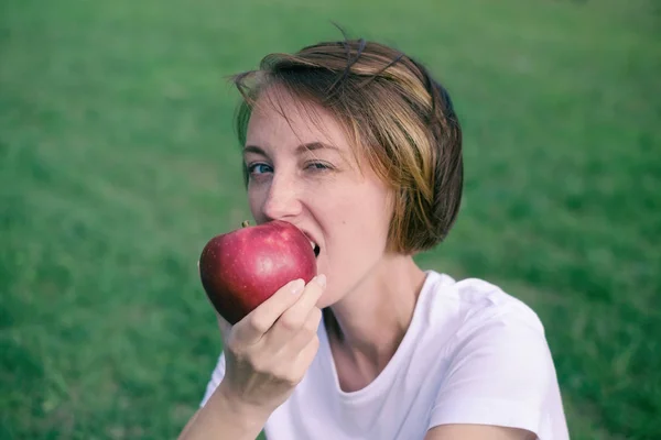 Sehr schönes kaukasisches Model isst roten Apfel im Park. — Stockfoto