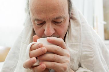 İhtiyar bir adamın kendini bir battaniye ile örtülü ve bir kupa tutan ben