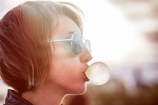 Ein Mädchen mit Sonnenbrille pustet eine Kaugummiblase. Nachdenken über das Leben. — Stockfoto
