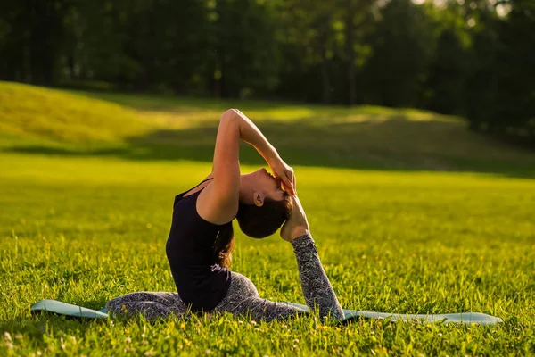 Eka Pada Rajakapotasana pose, on green suuny field in park. Side view — Stock Photo, Image