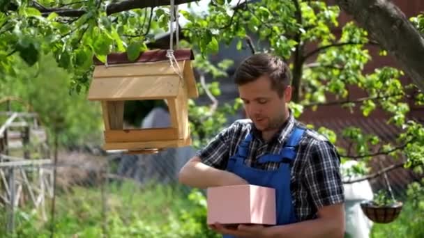 Молодой садовник в синем комбинезоне кормит птиц — стоковое видео
