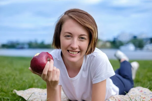 Modelo caucasiano muito bonito comendo maçã vermelha no Parque. Ao ar livre retrato de menina bonita — Fotografia de Stock