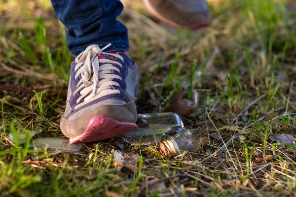 Γυναίκα πηγαίνει στο γρασίδι σε πάνινα παπούτσια. Κίνδυνος να περπατήσει σε ένα θραύσμα του σπασμένο μπουκάλι γυαλιού. — Φωτογραφία Αρχείου