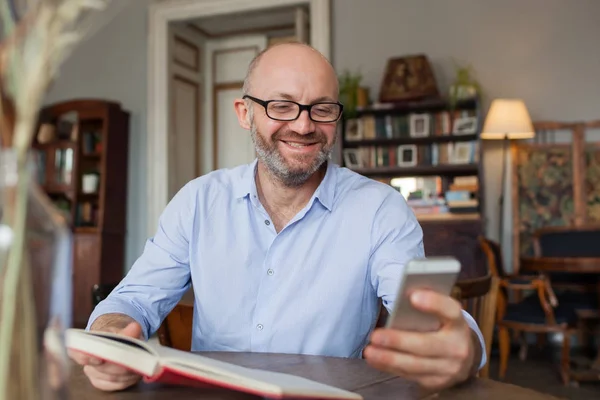 Человек читает книги в помещении и пользуется телефоном — стоковое фото