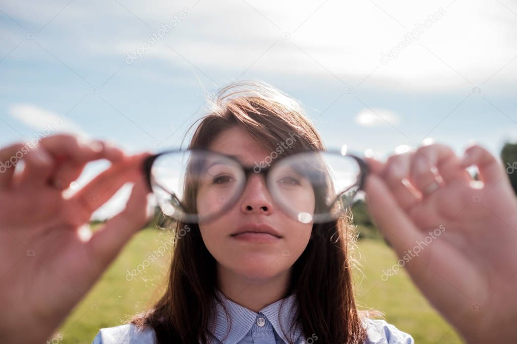 Young beautiful girl in shirt with long hair looks through glasses.