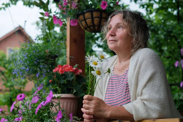 手に花を持つ緑豊かな庭園で年配の女性 — ストック写真
