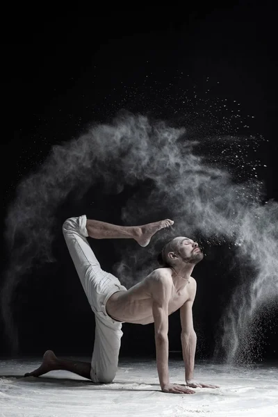 Een yoga leraar zit in een Sukkasana op een zwarte achtergrond. — Stockfoto