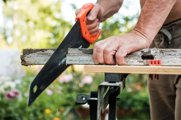 Kaukasische man werken Snij plank met handzaag buiten in de zomer. — Stockfoto