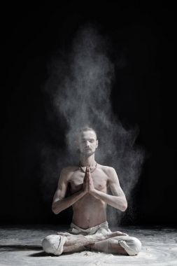 Bir yoga öğretmeni bir sukhasana siyah bir zemin üzerine oturuyor.