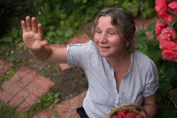 Cheerful mature woman sits in the garden and waving to friends — Stock Photo, Image