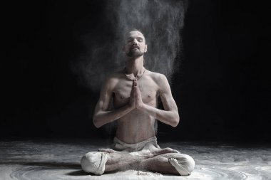 Bir yoga öğretmeni bir sukhasana siyah bir zemin üzerine oturuyor.