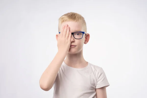 Niño rubio caucásico revisando la vista cerrando la mitad de la cara con la mano . —  Fotos de Stock