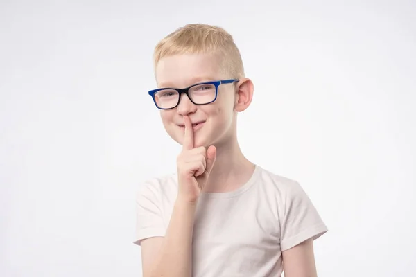 Young boy kid shows sign hand gesture holding finger on lips. — Stock Photo, Image