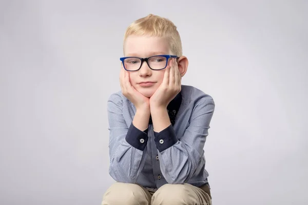 Porträt eines kaukasischen blonden Jungen mit Brille, der mit gelangweiltem Gesichtsausdruck vor die Kamera auf weißem Hintergrund blickt. — Stockfoto