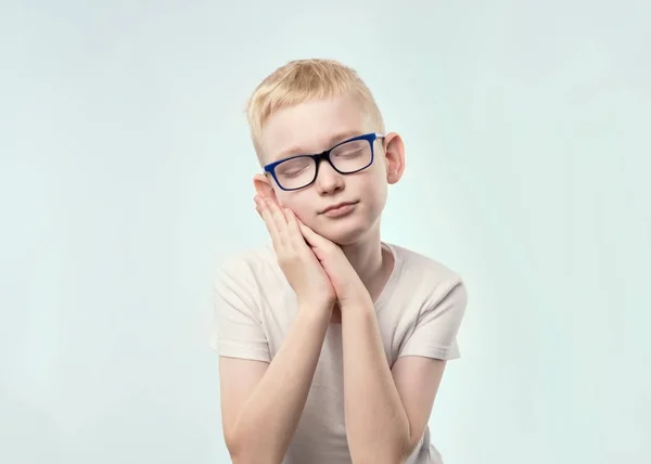 Porträt eines kaukasischen Jungen mit blonden Haaren. er schließt die Augen und hält die Hände wie ein Kissen, will schlafen. — Stockfoto