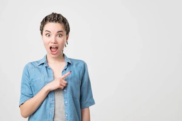 Caucasian woman surprise showing product .Beautiful girl with braids pointing to the side — Stock Photo, Image