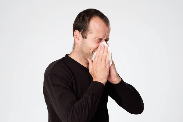 Volwassen man is ziek van de verkoudheid of longontsteking, niezen in servet. — Stockfoto