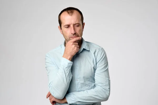 Homem caucasiano de camisa azul olhando para baixo com emoção cética no rosto . — Fotografia de Stock