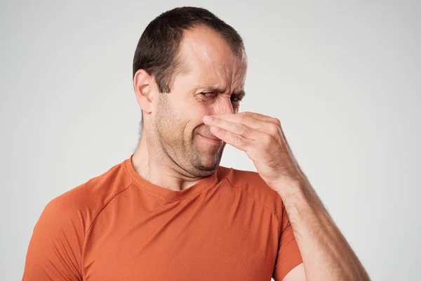 Kaukasischer Mann kneift Nase mit Fingern und schaut angewidert wegen schlechten Geruchs auf weißem Hintergrund — Stockfoto