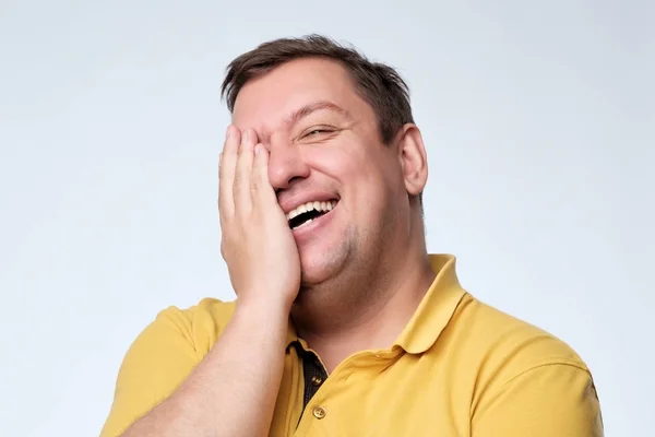 Kaukasische dikke man lacht en heeft betrekking op zijn gezicht met zijn handen. — Stockfoto