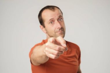 Beyaz adam turuncu tişört işaret parmağı size gülümseyen.