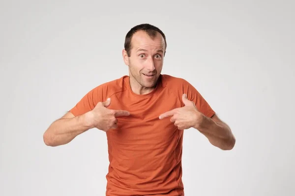 Um espanhol adulto em uma camiseta laranja aponta para si mesmo com o dedo . — Fotografia de Stock