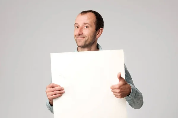 Hispánský muž drží znak prázdné studio bílé pozadí. — Stock fotografie
