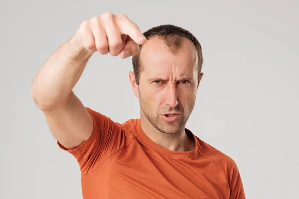 Mture man in oranje t-shirtfinger wijst naar de camera op een grijze achtergrond — Stockfoto