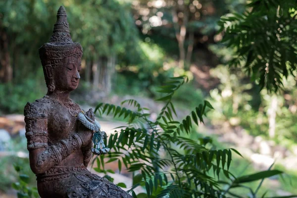 Uma estátua antiga de um buddha meditando contra um pano de fundo de uma floresta verde ou selva . — Fotografia de Stock