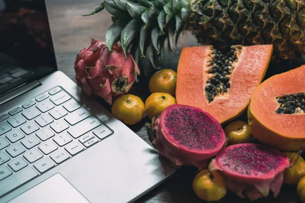 Тропические фрукты рядом с современным ноутбуком на деревянном фоне. Веганский образ жизни . — стоковое фото