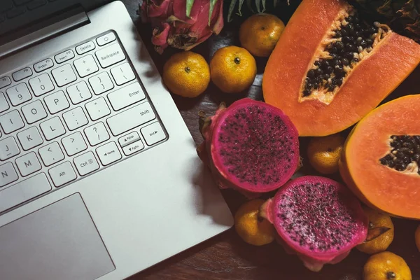 Tropisk frukt nära modern laptop på trä bakgrund. Vegansk livsstil. — Stockfoto