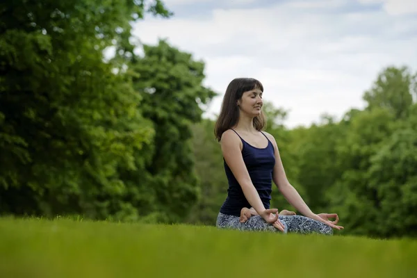 Beautiful young fit woman meditating, breathing, sitting with crossed legs in Lotus Posture in the park on summer day. — Stock Photo, Image