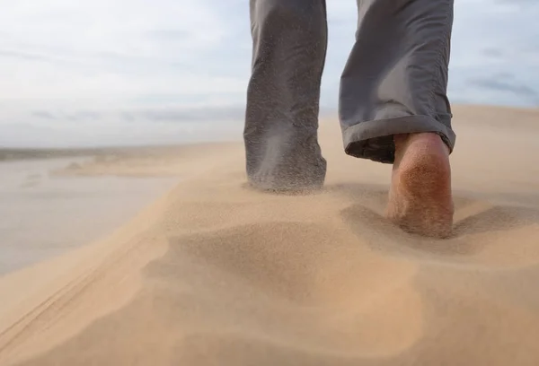 Un hombre camina por la playa de arena. En el aire, los granos de arena vuelan de un fuerte viento . —  Fotos de Stock