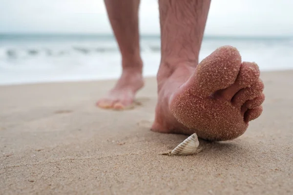 El hombre va a la playa y se va a poner de pie en la cáscara afilada rota . — Foto de Stock