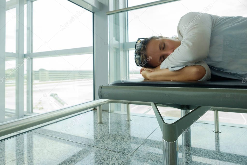 Tired passenger is sleeping o in airport terminal and waiting for airplane arrival.