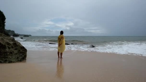 Mujer joven con impermeable amarillo en la playa bajo fuertes lluvias en Bali Indonesia — Vídeo de stock