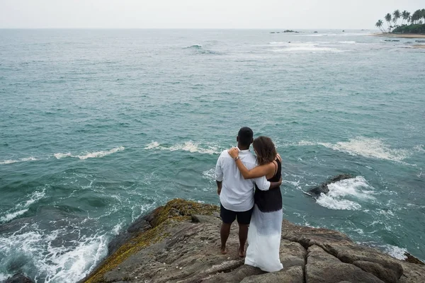 Just married couple on a trstone hugs and looks on the ocean water — Stock Photo, Image