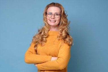 Çekici, gülümseyen, uzun saçlı ve elleri katlı, zarif bir kadın.