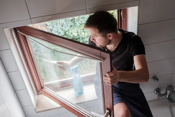 Άνθρωπος πλένει ένα παράθυρο σε ένα σπίτι χρησιμοποιώντας ξύστρα — Φωτογραφία Αρχείου