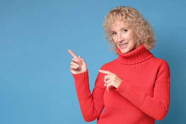 Дивовижна збуджена зріла стара жінка в червоному светрі, вказуючи на місце для копіювання — стокове фото