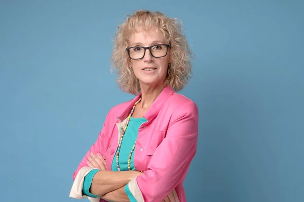 Mujer madura con el pelo rubio rizado y gafas sonriendo y de pie confiado — Foto de Stock