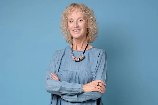 Modern elderly blonde woman standing smiling at the camera with folded arms — Stock Photo, Image