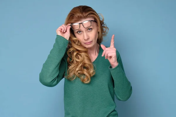 Зріла ділова жінка в окулярах вказує пальцем вгору — стокове фото