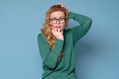 Mavi stüdyo arka planında tek başına duran olgun, korkmuş bir kadın..