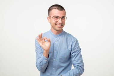 Gözlüklü, gülümseyen genç İspanyol adam onaylama sembolü gösteriyor..
