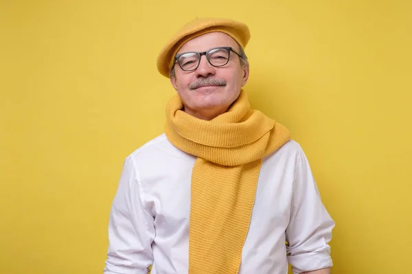 Hombre mayor hispano en boina amarilla y bufanda mirando con una sonrisa a la cámara . — Foto de Stock