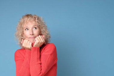 Mavi bir arka planda poz veren neşeli bir gülümsemesi olan yaşlı bayan.