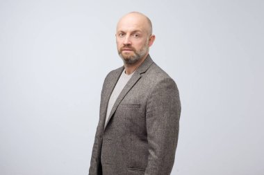 Sakallı, kendinden emin, olgun bir adam ciddi bir yüzle kameraya bakıyor..