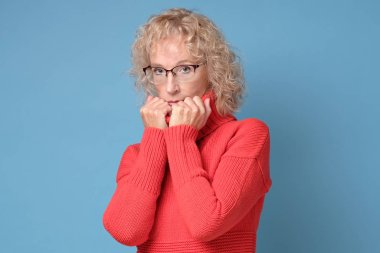 Mavi bir arka planda poz veren neşeli bir gülümsemesi olan yaşlı bayan.